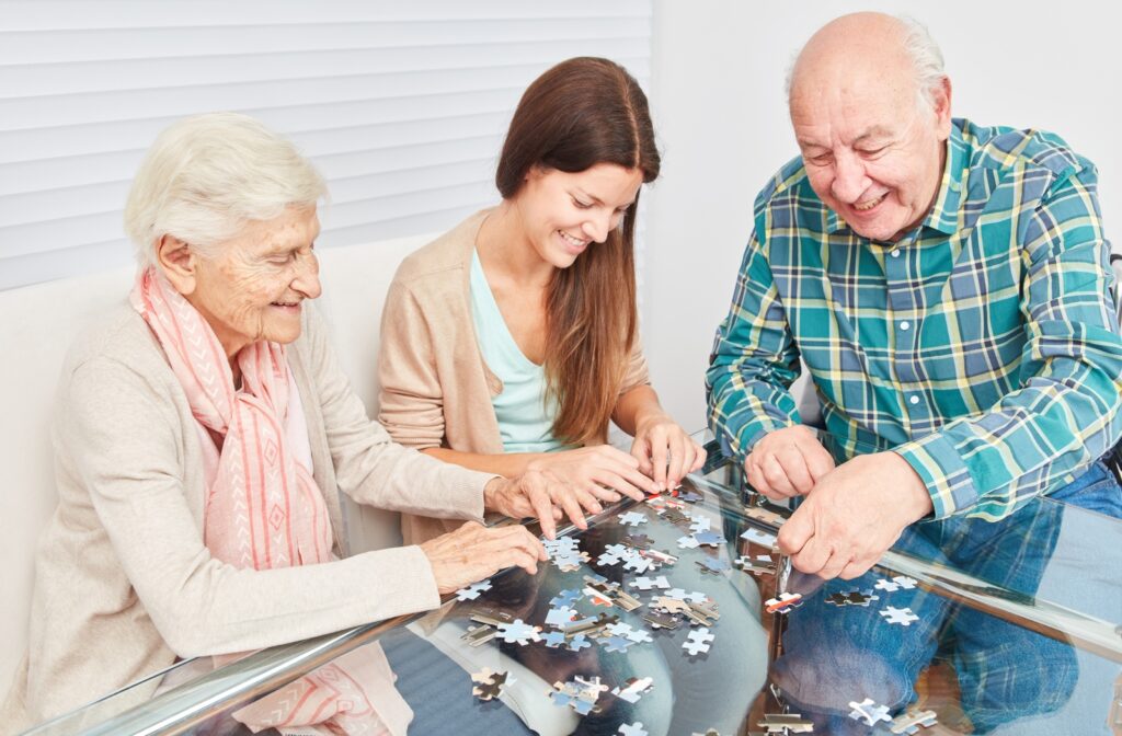 A senior couple doing a puzzle with a caregiver in a senior memory care community