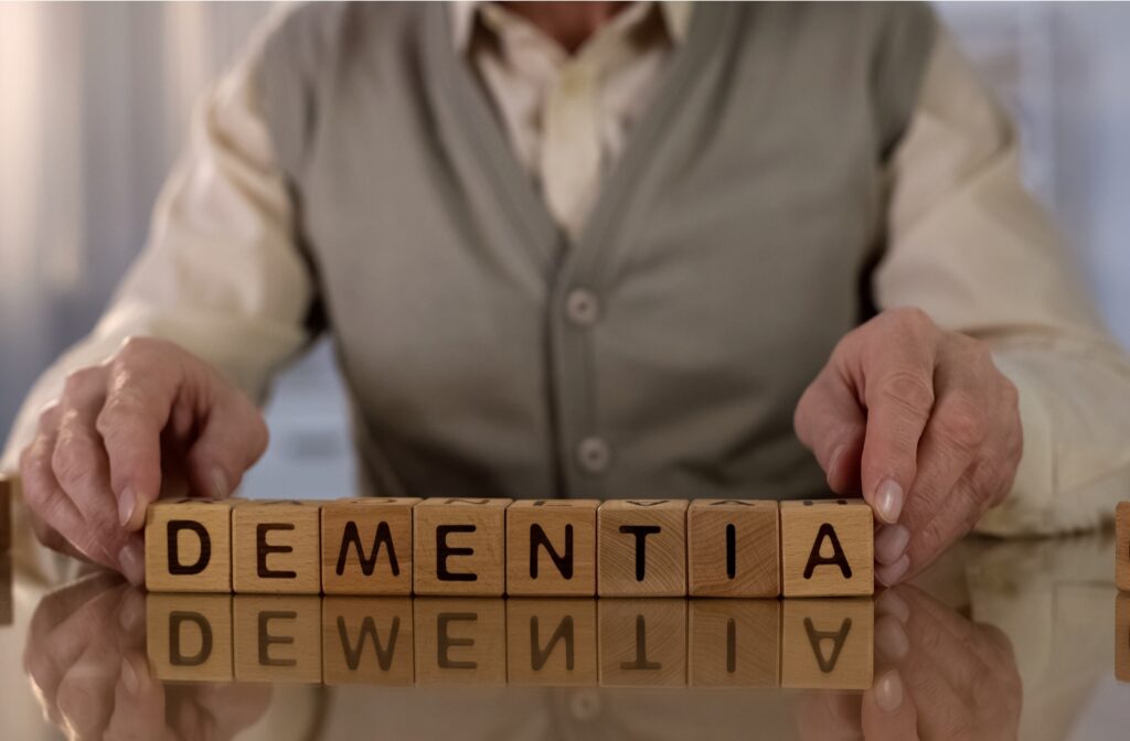 A senior man sitting at a table with small wooden blocks in front of him spelling out the word dementia