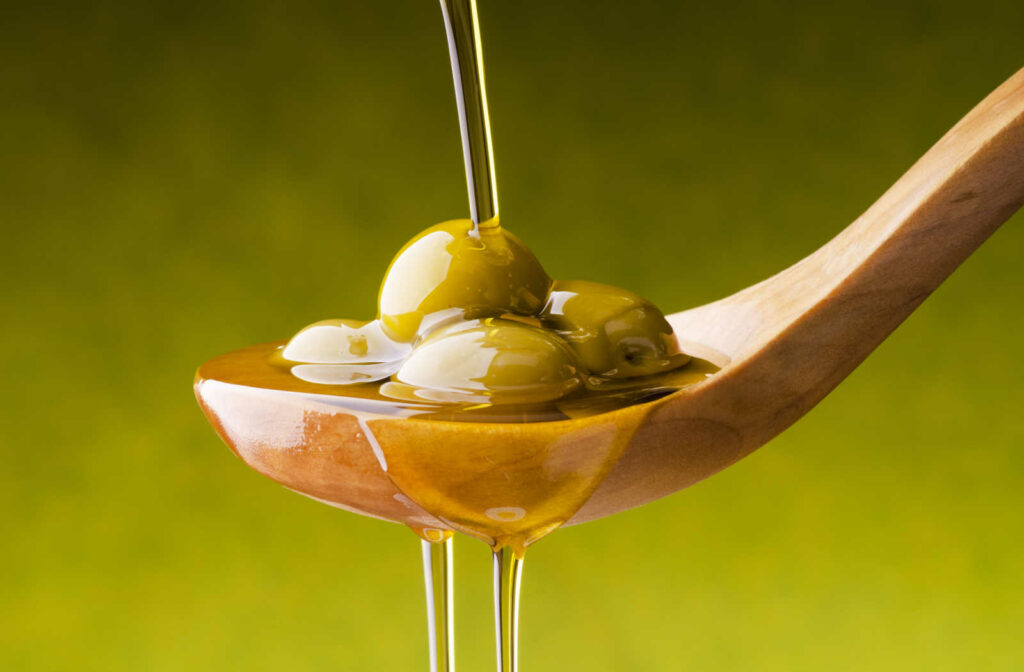 Extra virgin olive oil flows on a wooden bowl full of green olives.
