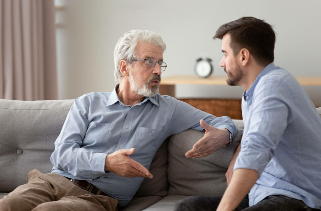 a senior man speaking to his middle aged son on a couch about memory care