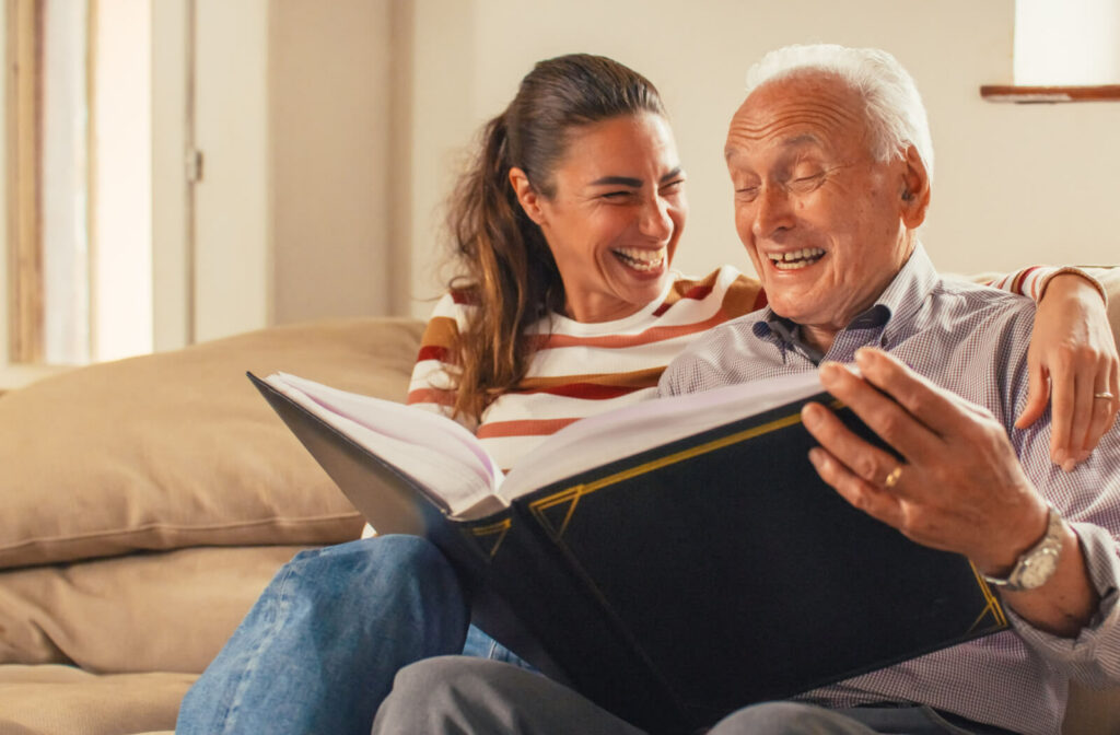 An older adult man and his daughter laughing while looking at a photo album together.